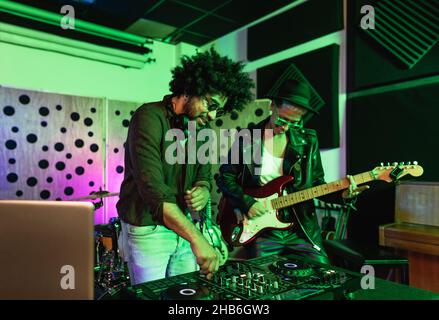 Junge glückliche Menschen spielen Musik mit dj-Mixer und Gitarre im Haus Produktionsstudio - Jugend Musiker Entertainment-Konzept Stockfoto