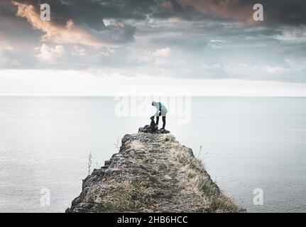 Rüde kuschelt Hund in der Natur vor dem Meer mit dramatischem Himmel im Hintergrund. Konzept der Freundschaft zwischen Tieren und Menschen. Stockfoto