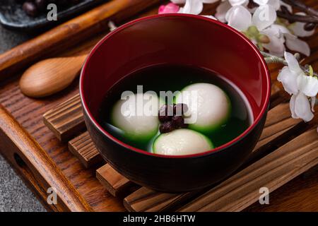 Nahaufnahme des großen Matcha tangyuan (tang Yuan) mit süßer Matcha-Suppe in einer Schüssel auf grauem Tischhintergrund für Festessen. Stockfoto