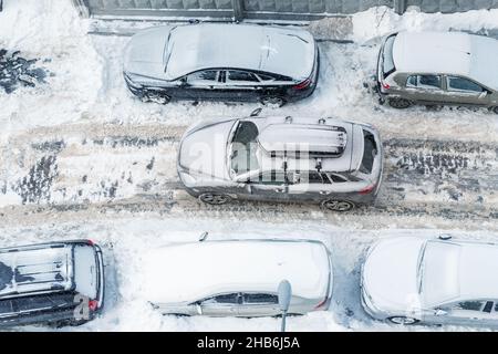 Oben über der Luftaufnahme eines modernen suv-Crossover-Fahrzeugs mit Dachgepäckträger, der durch Fahrzeuge fährt, die auf der von tiefem Schnee bedeckten Stadtstraße auf dem Klumpen geparkt sind Stockfoto