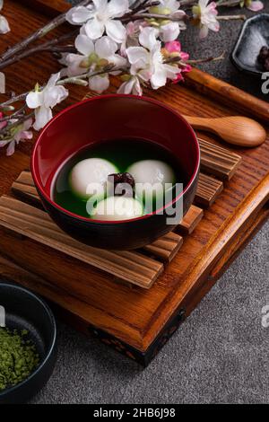 Nahaufnahme des großen Matcha tangyuan (tang Yuan) mit süßer Matcha-Suppe in einer Schüssel auf grauem Tischhintergrund für Festessen. Stockfoto