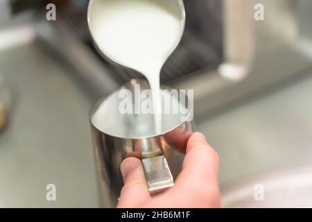 Ein Barista gießt geschlagene Milch aus einem Stahlkrug in einen anderen. Stockfoto