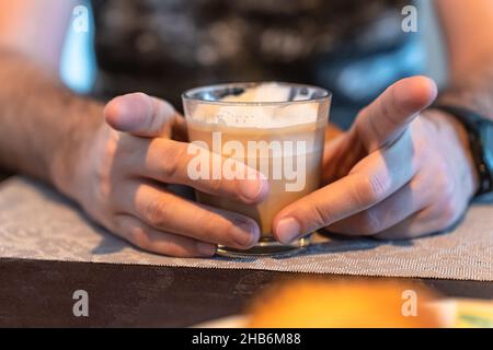 Selektive Konzentration auf die Hände eines Mannes, der ein Glas Cappuccino hält und seine Zeigefinger spreizen kann Stockfoto