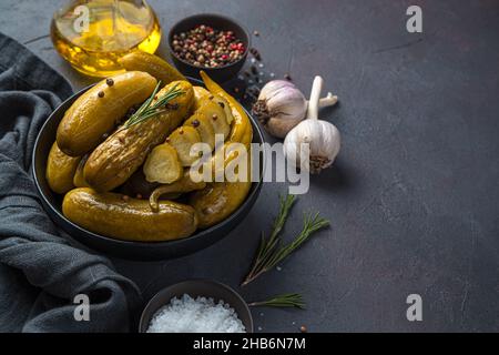 Eine Schüssel eingelegte Gurken mit Pfeffer und Rosmarin auf dunklem Grund. Seitenansicht, Kopierbereich. Stockfoto