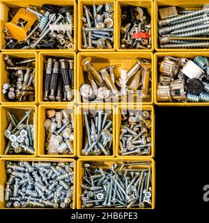 Gelbes Gehäuse mit kleinen Bauobjekten. Viele Staufächer gefüllt mit Bauherrenzubehör mit Schrauben, Muttern, Schrauben, Nägeln und Hafer Stockfoto