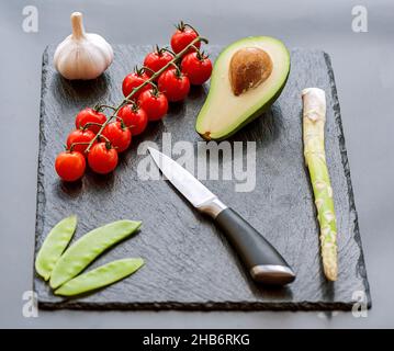 Männliche Hände, die die frische Avocado mit einem Küchenmesser des Küchenchefs auf einem mattschwarzen Schneidebrett schneiden. Gesundes Essen und Kochkonzept Stockfoto