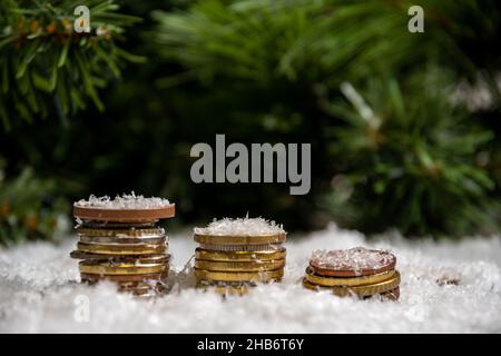 Eine goldene Pyramide von Münzen bedeckt mit Schnee vor einem Hintergrund von grünen Fichtenzweigen. Erfolgskonzept. Einsparungskonzept. Wohlstandskonzept im neuen Stockfoto