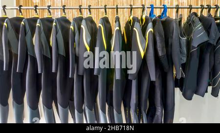 Eine Reihe von durchgehenden Neopren-Tauchanzügen, die in einem Resort-Tauchladen auf den Philippinen an einem Gestell hängen. Stockfoto