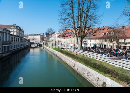 Ljubljana, Slowenien - 04 07 2018: Junge Menschen sitzen auf sonnigen Terrassen am Ufer des Flusses Ljubljana Stockfoto