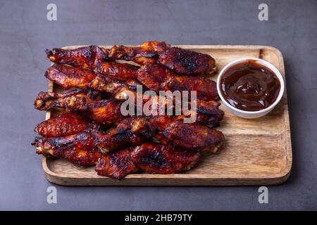 Gebratene Hähnchenflügel auf einem Holzbrett mit Grillsauce. Schwarzer Hintergrund, Nahaufnahme. Stockfoto