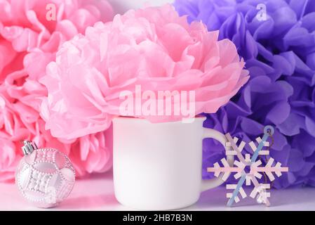 Weißer weihnachts-Mockup-Becher auf rosa und lila Papierblumen Hintergrund. Stockfoto