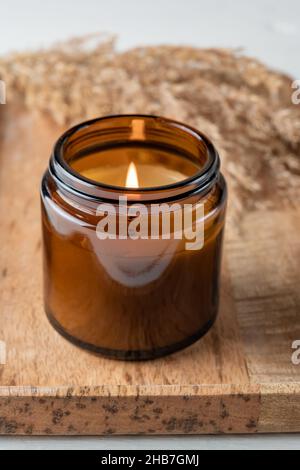 Brennende Duftkerze in einem Glas mit dem Aroma von Gewürzen. Herbststimmung mit trockenem Schilfgras. Gemütlicher Lebensstil. Stockfoto