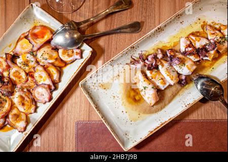 Direkt über einem Restauranttisch mit Platten gegrillter Tintenfische und Tintenfisch mit Olivenöl. Hochwertige Fotografie Stockfoto