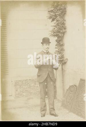 Porträt eines französischen Mannes mit einem Melone Hut, Beleuchtung einer Zigarette, Teil des Fotoalbums eines französischen Amateurfotografen mit Aufnahmen einer Familie, Brennerei Delizy &amp; Doistau Fils, der Armee und Sehenswürdigkeiten in Frankreich., anonym, Frankreich, c. 1900 - c. 1910, Papier, Albumin-Druck, Höhe 160 mm × Breite 114 mm Stockfoto