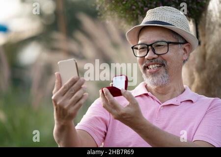 Happiness man Überraschung Ehe Vorschlag online an Freundin online durch Laptop-Computer. Graubart Ruhestand reifen oder Senior Mann in Pink und hat Stockfoto