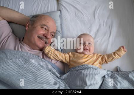 Fröhlicher Großvater, der sich morgens mit seinem Enkel auf dem Bett ausruhte und ein Nickerchen machte Stockfoto