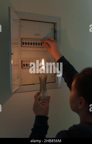 STROMAUSFALL: Frau hält eine Kerze im Dunkeln und versucht, die elektrische Schalttafel neu zu entfachen Stockfoto