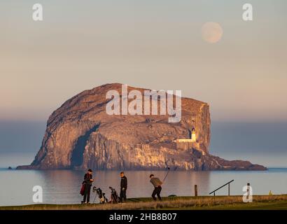 North Berwick, East Lothian, Schottland, Großbritannien, 17th. Dezember 2021. UK Wetter: Vollmond steigt über Bass Rock auf. Der Dezember-Vollmond wird als „Kalte Mond“ bezeichnet. Heute stieg es kurz vor Sonnenuntergang. Im Bild: Golfer genießen ein letztes Spiel, bevor die Sonne auf dem Golfplatz Glen untergeht Stockfoto