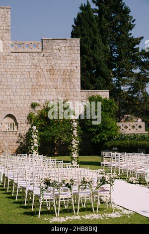 Der Halbbogen der Hochzeit steht in der Nähe einer Ziegelmauer im Garten vor einer Reihe von Stühlen Stockfoto