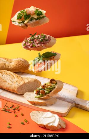 Kleine schwebender Baguette-Sandwiches auf einem leuchtend gelben und orangefarbenen Hintergrund mit grünen Blättern Stockfoto