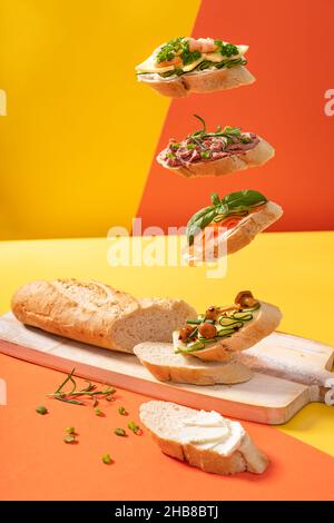 Kleine schwebender Baguette-Sandwiches auf einem leuchtend gelben und orangefarbenen Hintergrund mit grünen Blättern Stockfoto