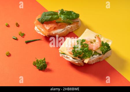 Kleine Baguette-Sandwiches auf hellem Gelb und Orange mit grünen Blättern Stockfoto