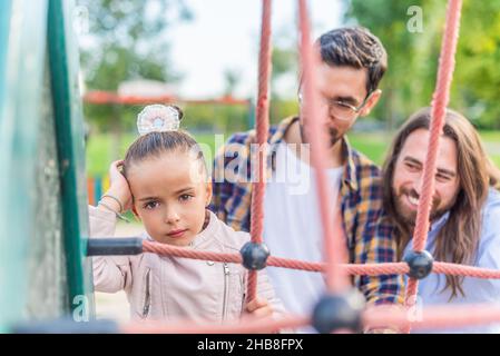 Mädchen auf dem Spielplatz mit ihren Eltern, die unglücklich auf die Kamera schauen. Stockfoto