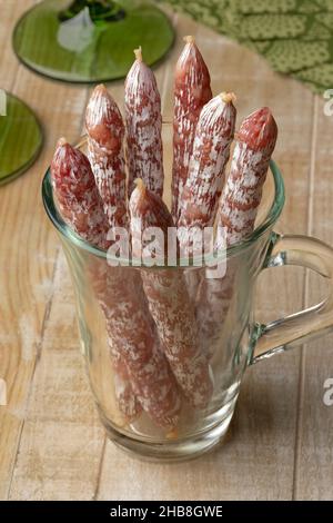 Glas mit trockenen geräucherten Salami-Sticks auf einem Holztisch für einen Snack aus der Nähe Stockfoto