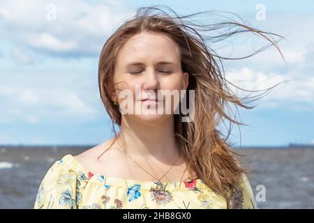 Ein großes Porträt einer jungen Frau mit flatternden Haaren im Wind an der Küste. Stockfoto