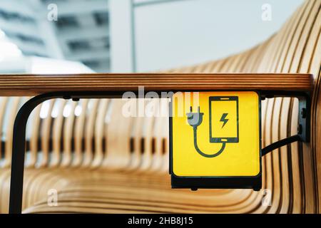 Eine Steckdose mit einem Geräteladeschild auf einer Holzbank am Flughafen. USB, Wireless, Stecker Stockfoto