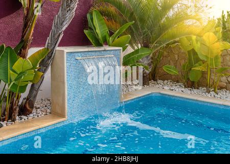 Nahaufnahme eines Wasserfalls in einem luxuriösen Pool in der Nähe des Hotels mit Palmen für Touristen. Sonniger Tag Stockfoto