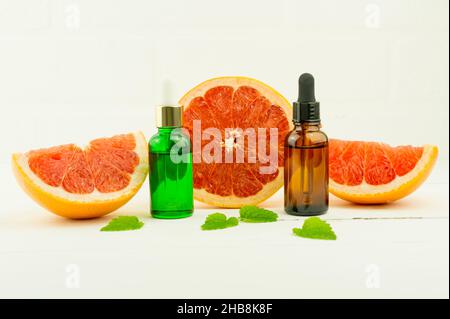 Vitamin C-Serum, eine Flasche ätherisches Bio-Grapefruitöl auf weißem Hintergrund mit Grapefruitscheiben und Zitronenmelisse. Stockfoto