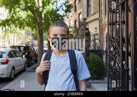 USA, New York, New York City, Porträt eines Jungen (8-9) in einer Gesichtsmaske, die auf dem Bürgersteig steht Stockfoto