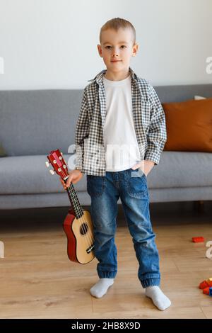 Talentiertes Kind mit Sopranukulele zu Hause. Vorschuljunge, der in Ruhe Gitarre lernt. Konzept der frühkindlichen Bildung und Musikhobby Stockfoto