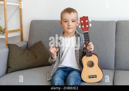 Talentiertes Kind mit Sopranukulele zu Hause. Vorschuljunge, der in Ruhe Gitarre lernt. Konzept der frühkindlichen Bildung und Musikhobby Stockfoto