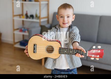 Talentiertes Kind mit Sopranukulele zu Hause. Vorschuljunge, der in Ruhe Gitarre lernt. Konzept der frühkindlichen Bildung und Musikhobby Stockfoto