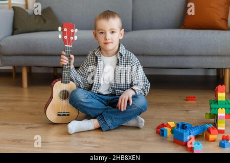 Talentiertes Kind mit Sopranukulele zu Hause. Vorschuljunge, der in Ruhe Gitarre lernt. Konzept der frühkindlichen Bildung und Musikhobby Stockfoto