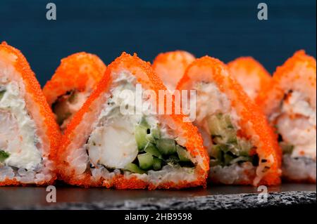 Dreieckige Fusion-Rollen mit orangefarbenem Tobiko-Rogen, Frischkäse, Garnelen und Gurken auf blauem Hintergrund in Nahaufnahme Stockfoto