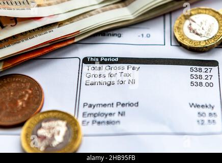 Ein Gehaltsnachweis, auf dem Sie mit einigen Banknoten und Münzen Steuerabzüge, nationale Versicherungen und Rentenbeiträge verdienen. Stockfoto