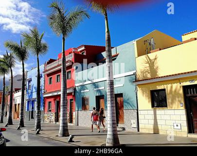 Bunte Häuser, eine gerade Reihe von Palmen und zwei Fußgänger in der Calle Mequinez in der Altstadt von Puerto de la Cruz, Teneriffa, Kanarische Inseln. Stockfoto