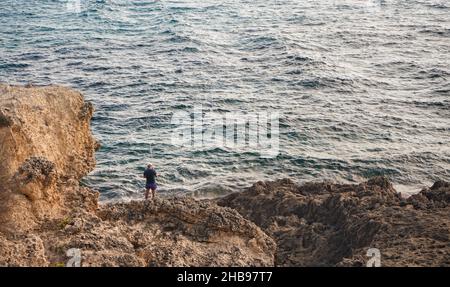 Einzelfischer, der am felsigen Ufer des Meeres steht, Blick von hinten Stockfoto