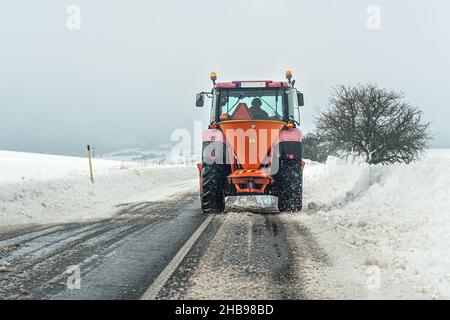 Kleiner Streuwagen-Wartungstraktor, der Eisensalz auf Asphaltstraße verteilt, Blick vom Auto, das dahinter fährt Stockfoto