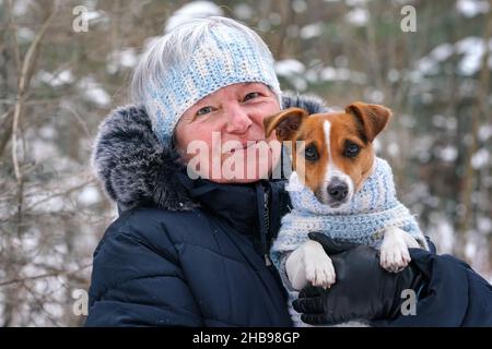 Ältere Frau, die einen kleinen Jack Russell Terrier Hund an den Händen hält, trägt einen passenden Strickpullover und ein Stirnband Stockfoto