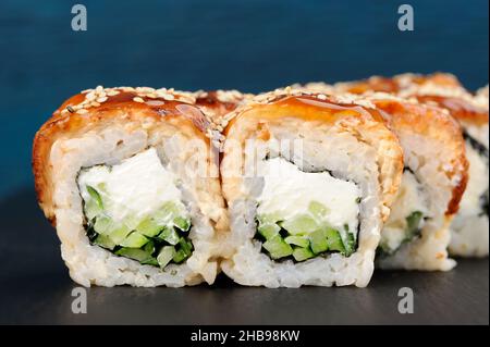 Leckere quadratische Sushi-Rollen mit Frischkäse und Gurken, bedeckt mit geräuchertem Aal und Karamellsoße aus der Nähe Stockfoto