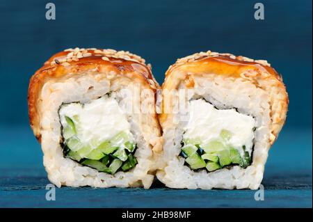 Sushi-Rollen mit Frischkäse, Nori und Gurken, bedeckt mit Aal und Karamell-Sauce auf blauem Hintergrund Nahaufnahme Stockfoto