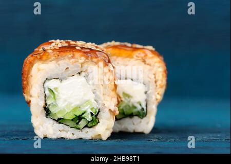 Sushi-Rollen mit Frischkäse, Nori und Gurken, bedeckt mit Aal und Karamell-Sauce auf blauem Hintergrund Nahaufnahme Stockfoto