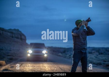 Fotograf, der in der Abenddämmerung in Utah vor dem Fahrzeug fotografiert Stockfoto