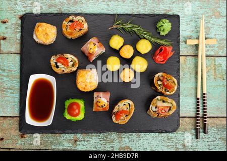 Set aus verschiedenen Rollen auf schwarzem Teller mit Sojasauce, Wasabi, Ingwer und Essstäbchen von oben Stockfoto
