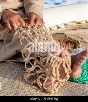 Der alte Mann strickt traditionelles Fischernetz, Hände und Füße in Rahmen Stockfoto