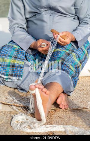 Der alte Mann strickt traditionelles Fischernetz, Hände und Füße in Rahmen Stockfoto